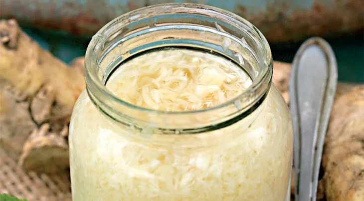 Тертый хрен в стеклянной банке, рядом ложка и корни хрена