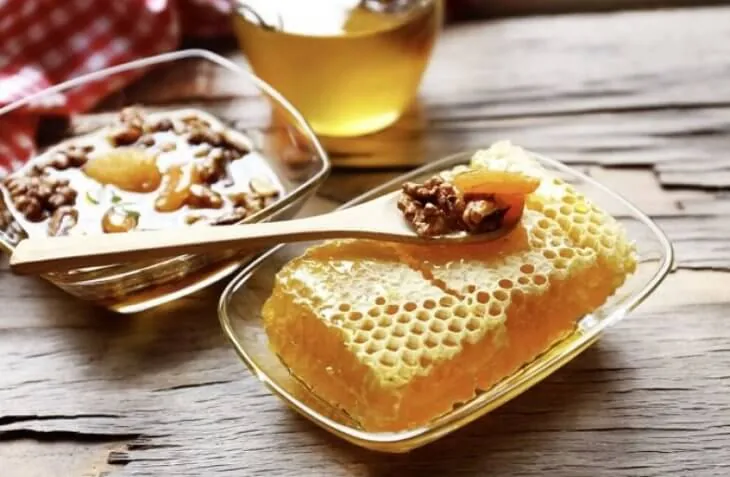 Кусок медовых сот, мед в пиале и ложка с орехами на деревянном столе