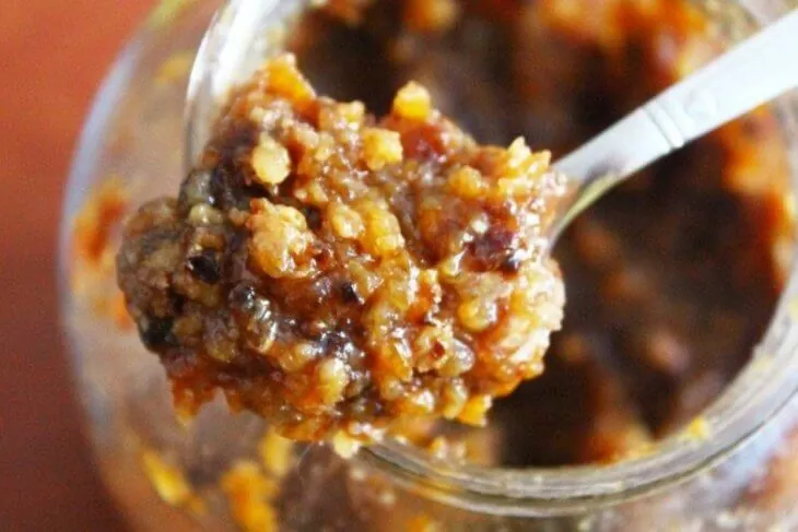 Ложка густой смеси меда с рублеными орехами и сухофруктами над банкой