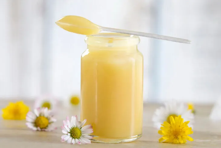 Баночка маточного молочка с ложечкой среди ромашек