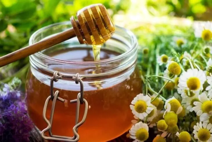 Банка меда рядом с цветками ромашки