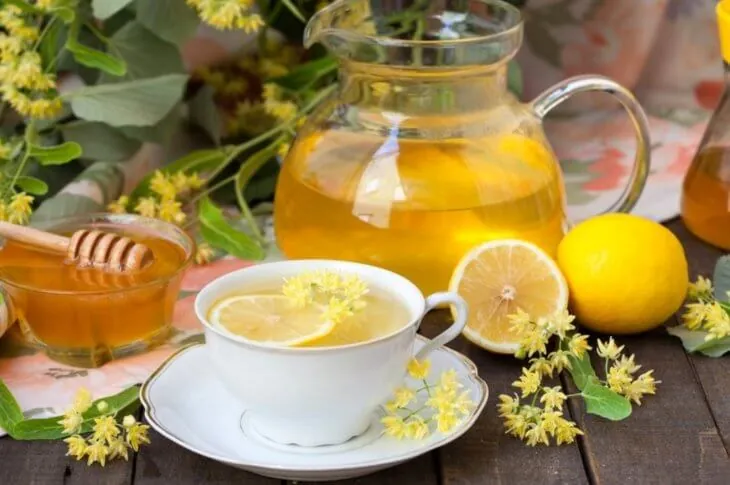 Чашка липового чая с лимоном, мед и цветки липы на столе
