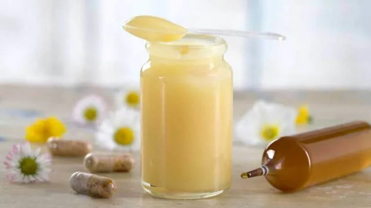 Банка маточного молочка, капсулы и флакон на столе с ромашками