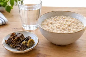 Кусочки прополиса-сырца на блюдце рядом с тарелкой овсяной каши и стаканом воды