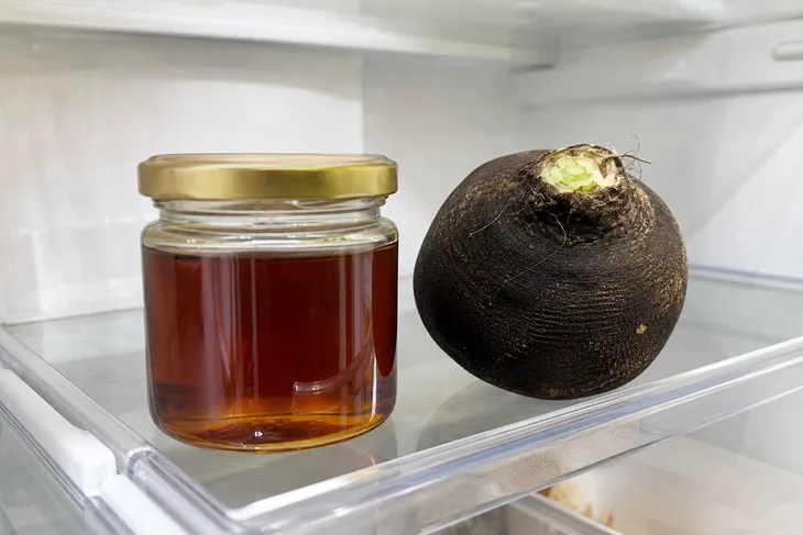 Закрытая банка с сиропом из редьки с медом на полке холодильника, рядом черная редька