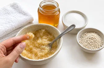 Миска с медово-сахарным скрабом, палец берет немного смеси, рядом банка меда, сахар, овсяная мука и полотенце