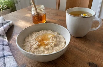 Тарелка овсяной каши с медом и чашка ромашкового чая на столе