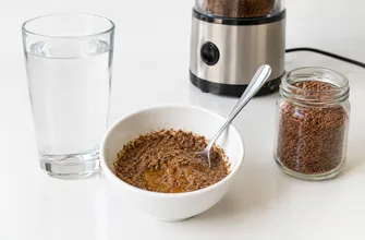 Порция молотого льна с медом в пиале, стакан воды и банка семян льна