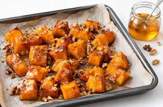 Кубики тыквы, запеченные с медом, корицей и грецкими орехами, на противне с пергаментом